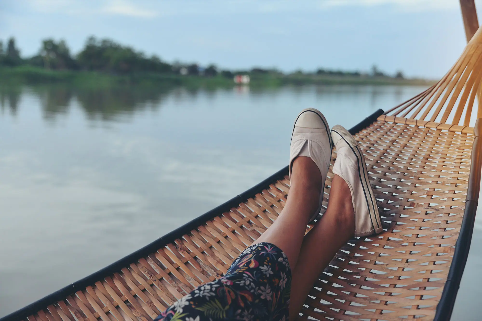 View of a lake with feet lounging in a hammock in the foreground